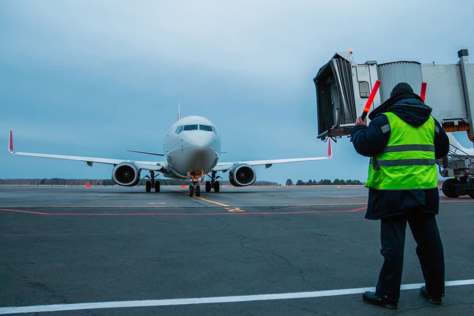 A ground-crew marshaller in a hi-vis vest guiding an airliner onto its stand