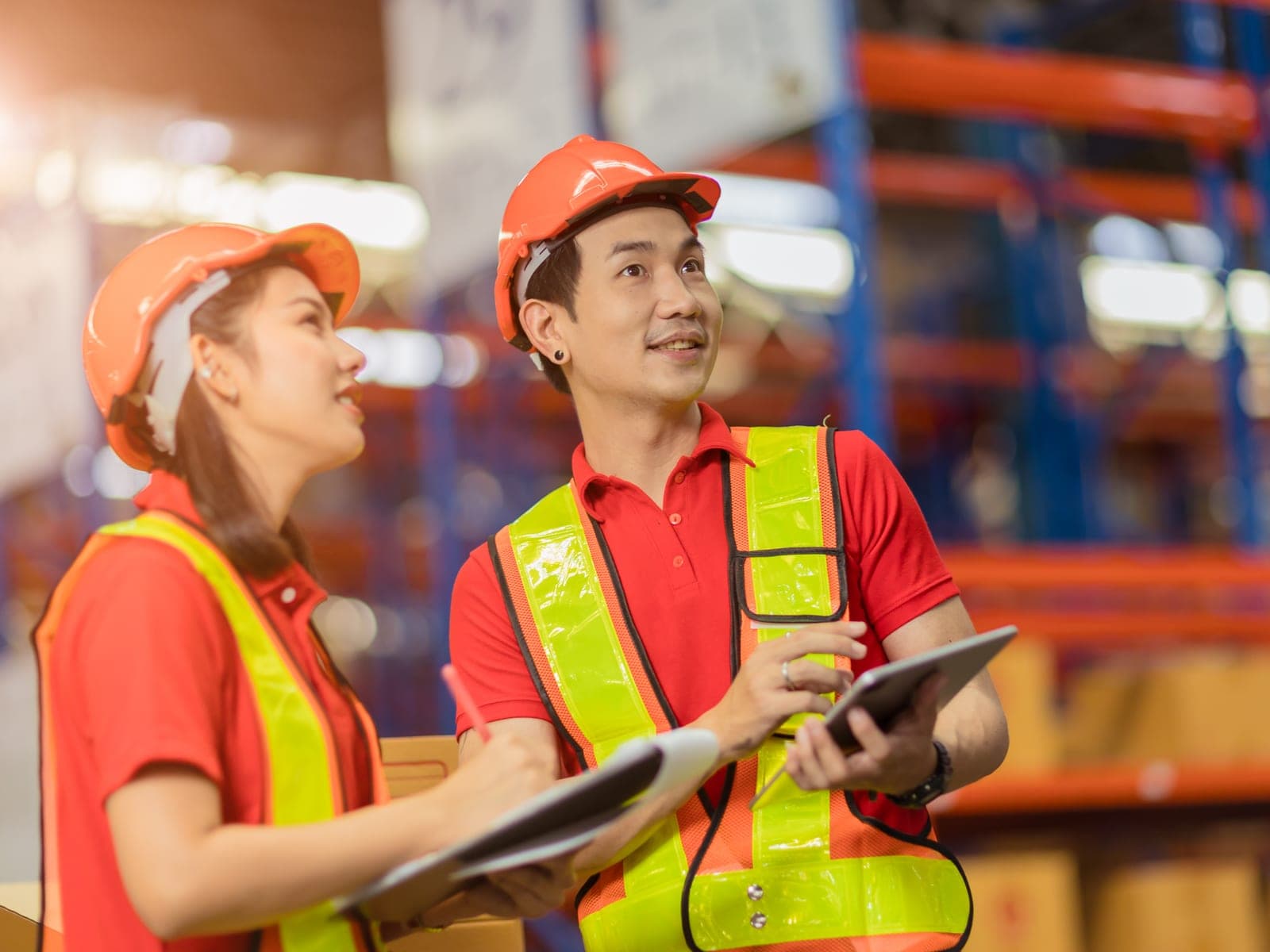 Two warehouse staff in hi-vis checking stock against a tablet and clipboard