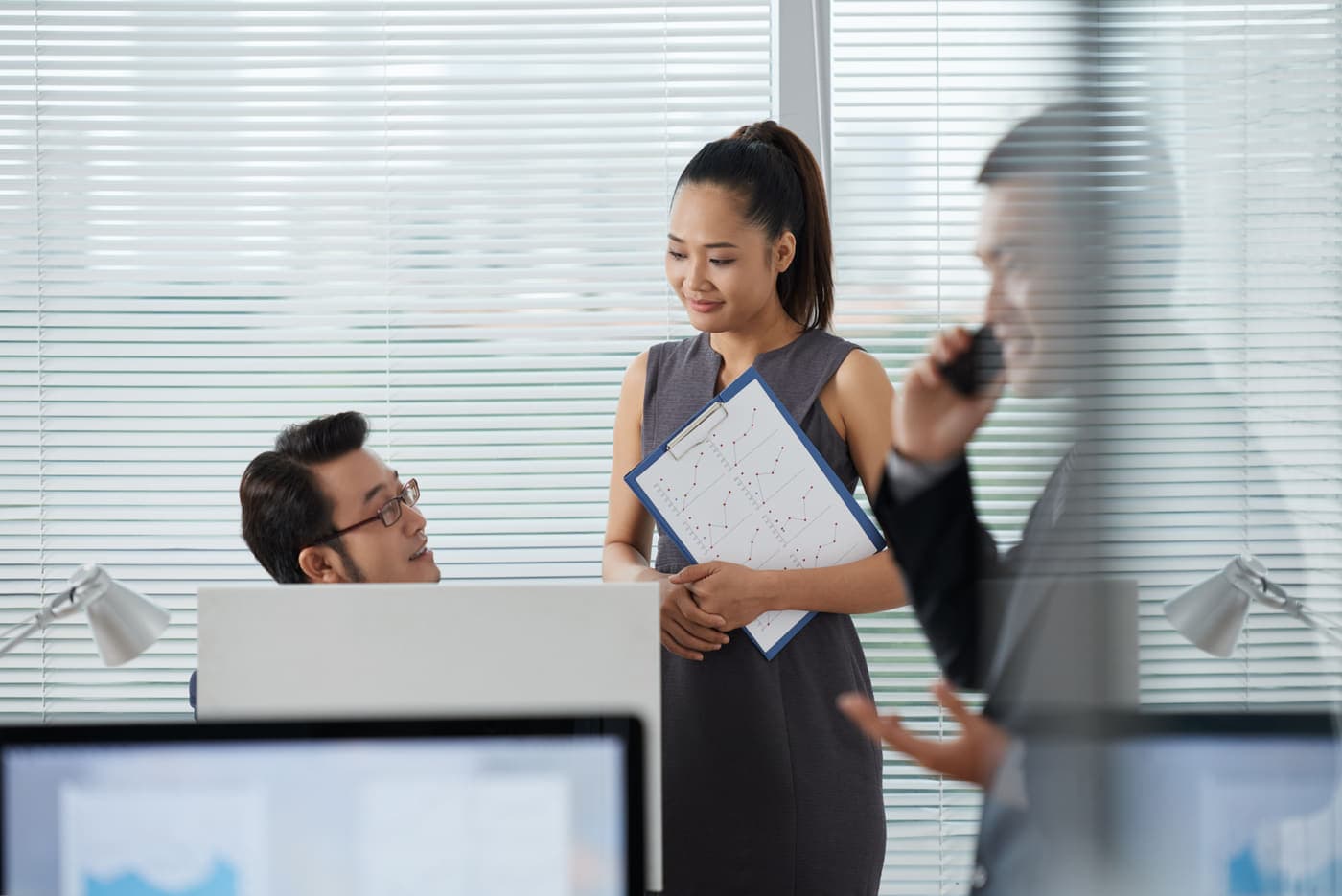 Colleagues talking over a desk in a bright office, one of them on a call