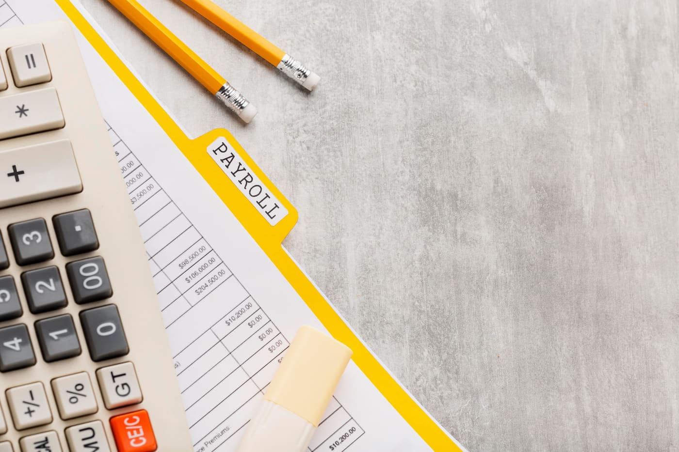 A payroll file, pay register and calculator laid out on a desk
