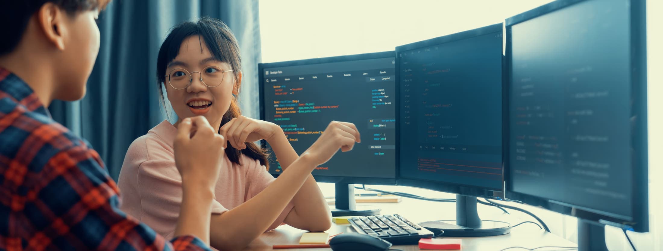 Two developers discussing code across a bank of monitors